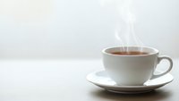 Hot steaming tea cup on white saucer against neutral background for morning beverage and relaxation concepts.