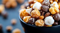 Assorted chocolate candies and nuts in black ceramic bowl on dark background, selective focus on sweet treats with caramel, white chocolate and sesame coating.