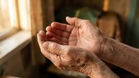 Elderly hands cupped in prayer or receiving gesture, wrinkled skin showing age and wisdom, warm natural lighting from window creating peaceful atmosphere.