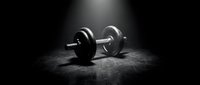 Single chrome dumbbell on dark textured surface with dramatic spotlight lighting, suitable for fitness, gym, and workout design projects.