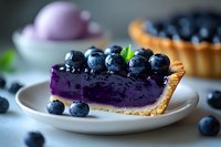 Fresh blueberry pie slice with vibrant purple filling garnished with whole berries and mint leaves on white plate, selective focus macro shot for food photography.