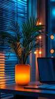 Atmospheric home office workspace with glowing orange planter and palm plant against blue-lit window blinds, laptop on desk, creating cozy evening ambiance.