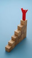 Red figure with raised arms standing on top of wooden block staircase against blue background, symbolizing success, achievement, leadership and career growth for business concepts.