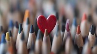 Red heart shape among colorful wooden pencils in creative arrangement, shallow depth of field composition showing love for art and creativity concept.