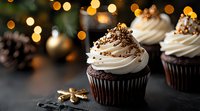 Chocolate cupcakes with vanilla frosting and golden sprinkles against blurred Christmas lights and decorations create festive holiday mood on dark background.