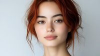 Young woman with auburn hair and natural makeup against light background, showcasing freckles and soft features for beauty, fashion, or lifestyle content.