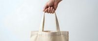 Male hand holding a blank beige canvas tote bag on white background, mockup for branding, eco shopping, and sustainable design projects.