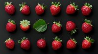 Fresh ripe strawberries and green leaf arranged in rows on black background, top view. Natural organic berries pattern for healthy food design.