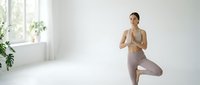 Young Asian woman practicing tree pose yoga in bright minimalist room with natural light and plants for wellness meditation and mindfulness exercise.