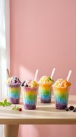 Colorful layered shaved ice drinks with rainbow gradient effect, topped with fruit and cream, arranged on wooden table against pink wall background.