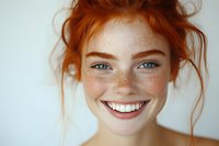 Young woman with natural red hair, freckles and bright blue eyes smiling genuinely at camera against white background. Fresh-faced natural beauty portrait.