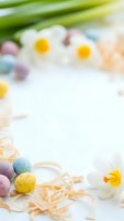 Easter background with colorful eggs, white daffodils and green tulips on light surface with copy space for spring holiday greeting cards and decorations.