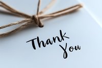 Handwritten thank you note on white paper with rustic twine bow, elegant calligraphy style lettering in black ink creates minimalist gratitude message.