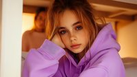 Young woman in purple hoodie with messy bun hairstyle and natural makeup poses during golden hour sunlight, creating moody atmospheric portrait with warm tones.