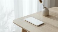 Smartphone with blank white screen on wooden table beside ceramic vase, minimal Scandinavian interior, natural light, mockup for app or web design.