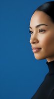 Young woman of Asian descent in profile view wearing black turtleneck against solid blue background. Suitable for corporate, beauty, wellness and professional headshot applications.