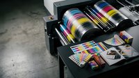 Professional offset printing press with CMYK ink rollers and color calibration charts for commercial print production and quality control processes.