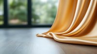 Elegant golden silk fabric draped on wooden surface creates soft waves and folds with natural window lighting, adding luxurious texture and depth to interior setting.