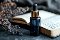 Dark blue glass dropper bottle with essential oil placed on open book with dried lavender sprigs, moody atmospheric composition on textured stone background.