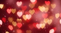 Romantic heart-shaped bokeh lights in warm red and pink tones create dreamy Valentine's Day atmosphere with soft glowing effects and sparkling background.