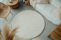 Cozy round white fluffy carpet on gray floor with pampas grass decor and furniture elements in modern minimalist interior design style.