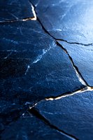 Deep blue cracked surface with golden light seeping through fissures creates dramatic contrast and texture, highlighting natural fracture patterns in stone.