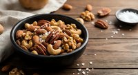 Mixed nuts assortment in black bowl on rustic wooden table with sea salt. Healthy snacking, cooking ingredients for recipes and nutritional food concept.