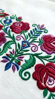 Colorful floral embroidery on white fabric featuring red roses, green leaves and decorative swirls in traditional folk art style for textile and craft projects.