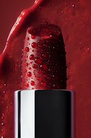 Red lipstick with water drops macro photography on dark background. Luxury cosmetic product with moisture effect for beauty and fashion advertising.