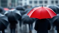 Red umbrella standing out in crowd of people with black umbrellas on rainy city street, representing uniqueness, leadership and individuality in business concept.