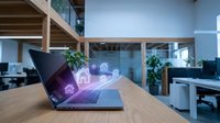 Modern laptop displaying digital home automation icons on wooden desk in contemporary office workspace with glass partitions and plants.