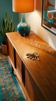 Mid-century modern entryway with wooden sideboard, teal lamp, welcome sign, and vintage keys, evoking warm retro home decor style.
