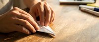 Close-up of hands turning pages of an open book on wooden desk with writing supplies nearby, suitable for education and reading concepts.