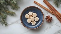 Homemade white chocolate candies on blue ceramic plate with winter spices, star anise, cinnamon sticks and pine branches on marble background.