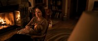 Young woman relaxing in cozy living room by fireplace with warm lighting, reading book in comfortable armchair during evening at home.