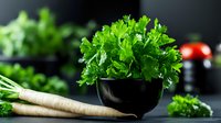 Fresh parsley leaves in black ceramic bowl and raw parsnip roots on dark background, selective focus. Cooking healthy vegetarian food concept.