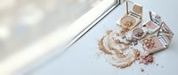 Luxury rose gold makeup powder spilled from elegant compact mirror creating artistic beauty mess on white marble surface for cosmetic branding.