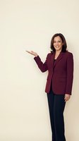 Professional mixed-race businesswoman in burgundy blazer presenting with open palm gesture against neutral background for corporate communications.