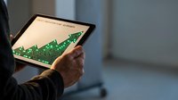 Professional engineer analyzing electronic circuit board design on digital tablet in modern office environment for technology development projects.