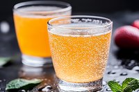 Refreshing apple cider glasses with bubbles and condensation, served with fresh mint leaves and red apples on dark background.