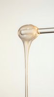 Honey dripping from metal spoon against neutral background, showcasing golden liquid texture and viscosity for food, culinary, and ingredient content.
