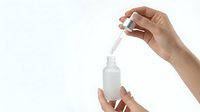 Hand holding dropper bottle applying serum or essential oil on white background isolated for skincare and beauty product design.