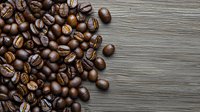 Fresh roasted coffee beans scattered on rustic gray wooden background with copy space, overhead view showing rich brown color and natural texture.