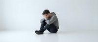 Young man sitting alone on floor holding head in hands showing depression anxiety stress mental health struggles emotional pain isolated white background.