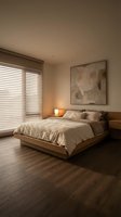 Serene bedroom interior with wooden platform bed, neutral bedding, warm lighting from nightstand lamp, horizontal blinds at window, and abstract wall art.