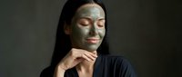 Young Asian woman with green clay facial mask, eyes closed, relaxed expression, dark background, skincare and beauty treatment concept.