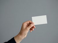 Young adult male hand with medium skin tone holding blank white business card against neutral gray background, suitable for corporate branding, marketing materials, and business presentations.