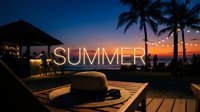 Straw hat and sunglasses on wooden table at tropical beach bar during sunset with glowing summer text overlay and palm trees.