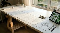Artist workspace with botanical sketches spread on wooden desk near bright window for creative design projects.