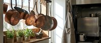 Copper pots and pans hanging in rustic kitchen with herbs on wooden shelf. Traditional cookware display for culinary cooking and home decor concepts.